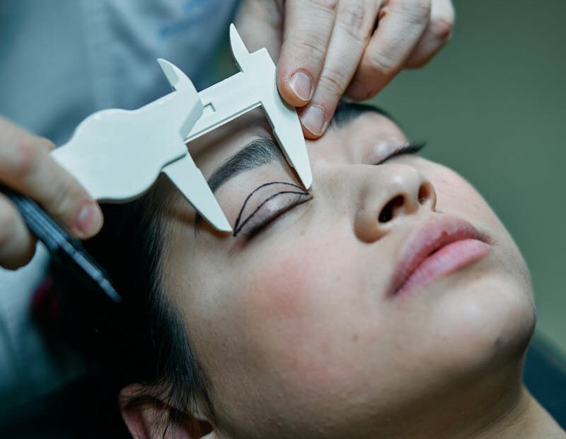 A surgeon measures a patient's eyelid for blepharoplasty preparations.
